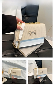 Detail of white leather and beige weave crossbody bag with metal bow and gold chain strap