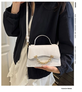 Detail of white crocodile embossed handbag featuring bold gold chain and flap closure