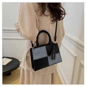 Detail of a minimalist square tote bag featuring black leather and grey textured patchwork