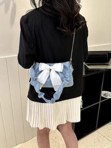 Detail of light blue pleated shoulder bag featuring a white bow and chain strap