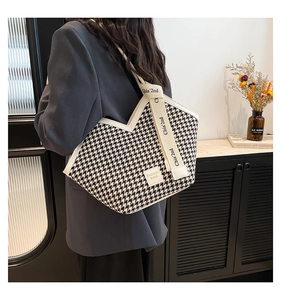 Macro detail of houndstooth tote bag showing white leather trim and logo lettering
