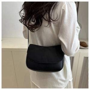 Minimalist black leather crossbody flap bag shown on model in a soft cream indoor setting