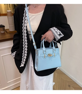 Detail of light blue crossbody bag with gold hardware and turn-lock closure on strap