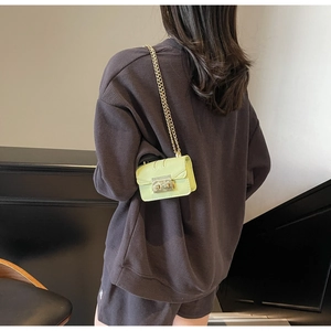 Détail du mini sac chaîne vert citron avec fermoir doré porté sur un sweat gris texturé
