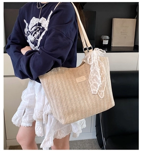 Detail of V-shaped woven straw tote featuring white lace bow and adjustable leather strap