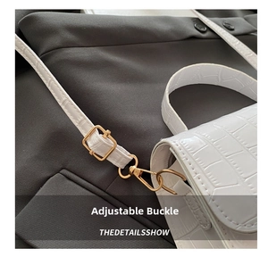 Close-up of golden adjustable buckle and lobster clasp on white crocodile pattern handbag