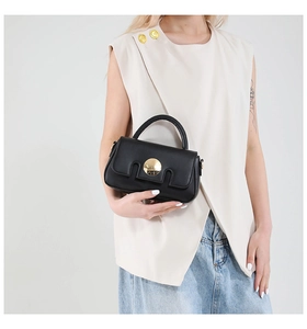 Detail of a black leather mini handbag featuring a prominent gold circular magnetic buckle