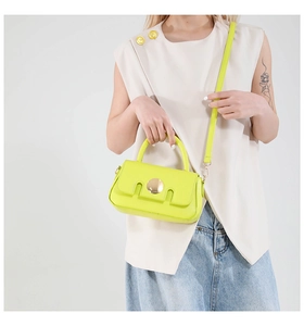 Detail of neon green crossbody bag featuring a large round gold metal clasp and leather texture