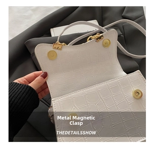 Detail of white crocodile pattern bag featuring double gold magnetic snap closures