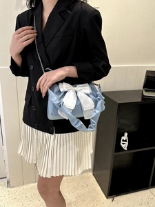 Close-up of light blue shoulder bag featuring a large white satin bow and stylish pleats