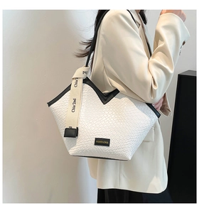 Close-up of woven tote bag with V-shaped leather trim and fashion brand nameplate