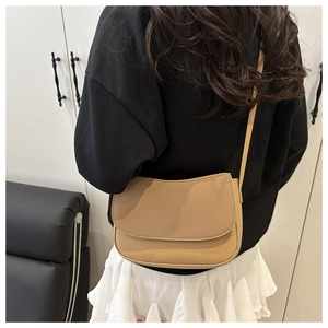 Detail of khaki leather shoulder bag with flap closure worn by a model in interior setting