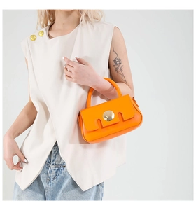 Close-up of bright orange crossbody bag with gold round metal clasp on a model
