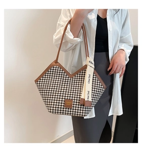 Detail of houndstooth tote bag with brown leather handles and white logo ribbon strap
