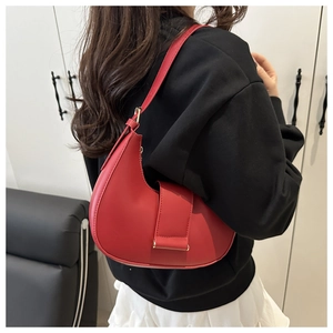Detail of red crescent-shaped leather underarm bag with gold buckle and smooth matte finish