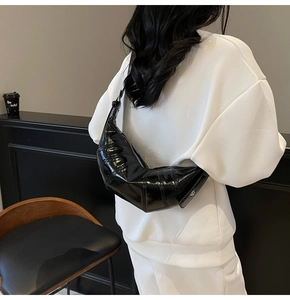 Detail of black patent leather croissant bag with quilted pattern worn by a model