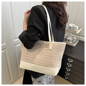 Detail of large woven straw tote bag with white leather contrast shoulder strap on a model