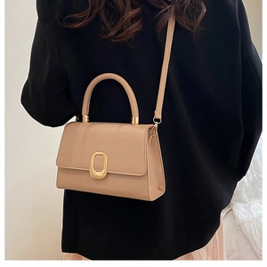 Close-up of beige crossbody bag with textured gold clasp on black blazer outfit