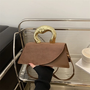 Sac à main marron avec poignée dorée sculpturale posé sur une chaise moderne chic
