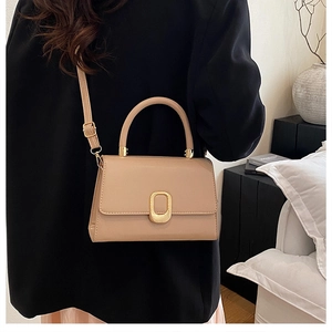 Close-up of beige minimalist crossbody bag featuring a luxury gold buckle and top handle