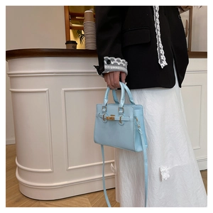 Detailed shot of a light blue faux leather handbag with golden twist lock and shoulder strap
