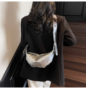 Silver croissant bag with quilted design and wide shoulder strap shown on a model
