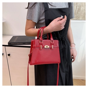 Close-up of red patent leather tote bag featuring a metallic turn-lock and double handles