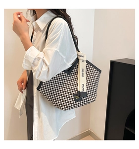 Detail view of large houndstooth tote bag featuring black leather trim and woven logo strap