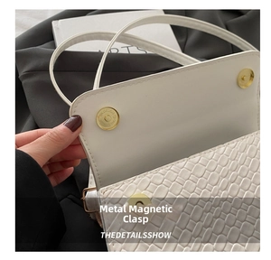 Macro shot of white textured shoulder bag featuring gold magnetic clasp closure details
