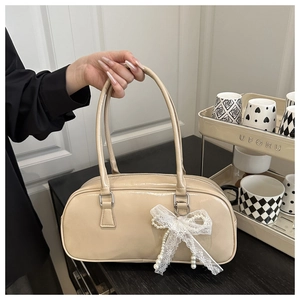 Detail of beige patent leather handbag with delicate lace bow and pearl pendant charm