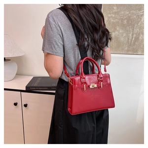 Close-up of lifestyle use showing red glossy handbag with metal twist-lock and shoulder strap