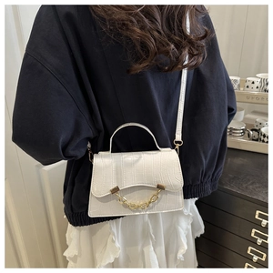 Detail view of a white crocodile texture crossbody bag with gold chain and top handle