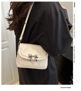 Detail shot of a cream-colored crossbody bag featuring a metallic silver bow ornament