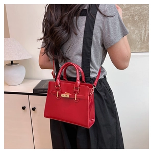 Detailed back view of a woman wearing the bright red glossy handbag with golden buckle belt