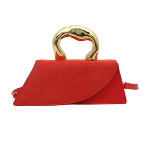 Red suede tote bag with artistic gold metal handle and slim shoulder strap on white backdrop
