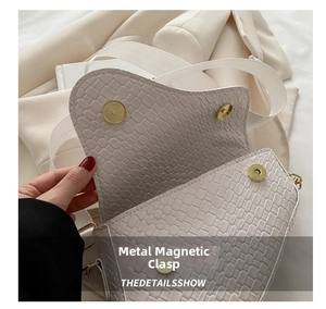 Detail of cream crossbody bag featuring faux crocodile texture and dual magnetic snaps
