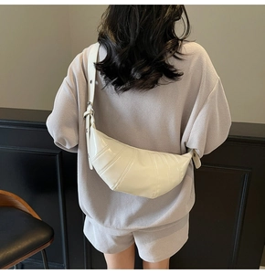 Detail of white glossy croissant bag featuring stitching design and wide shoulder strap