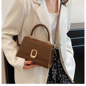 Close-up of brown leather bag featuring an elegant gold oval metal buckle and top handle