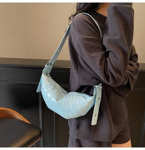 Close-up of light blue croissant bag with segmented stitching and wide shoulder strap