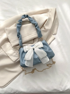 Detail of light blue pleated handbag featuring a large white bow and golden chain strap