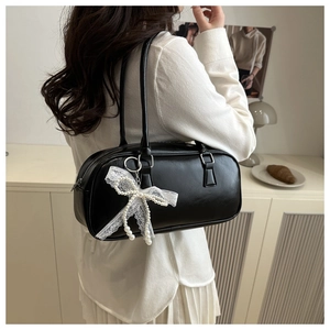 Detail of black leather pillow bag featuring white lace and pearl bow charm accessory