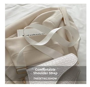 Detail of white crocodile texture saddle bag featuring wide fabric strap and gold buckle