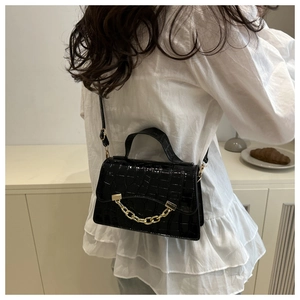 Detail of black crocodile pattern handbag with gold chain accent and slim strap