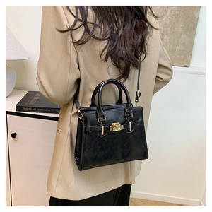 Close-up of black leather handbag with gold hardware lock and strap on model side view
