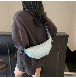 Detail of light blue glossy leather crescent bag with curved stitching and shoulder strap