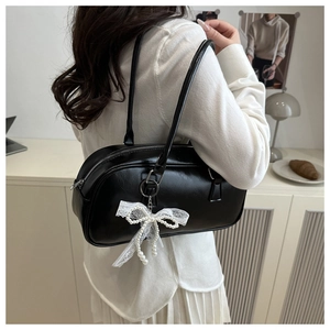 Detail of black glossy pillow bag with white lace and pearl bow charm on shoulder