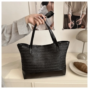 Close-up of a black woven tote bag featuring a leather bottom panel and slim shoulder straps