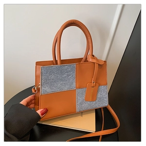 Detail of trendy brown faux leather and grey denim patchwork bag with gold metal buckle