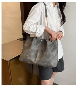 Detail of dark gray leather tote bag with metal chain strap and vertical stitching accents