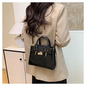 Side view of black leather handbag with gold twist lock on beige blazer outfit